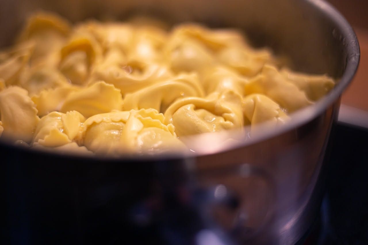 Ciotola di porcellana bianca con anolini pieni di ripieno scuro, immersi in brodo trasparente e freddo, decorati con prezzemolo fresco e scaglie di parmigiano