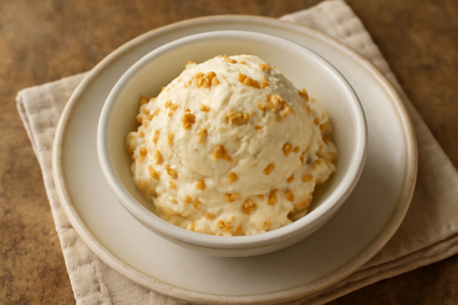 Gelato avorio cremoso con frammenti croccanti di torroncino marrone in una coppetta trasparente, guarnito con una nocciola intera sulla superficie