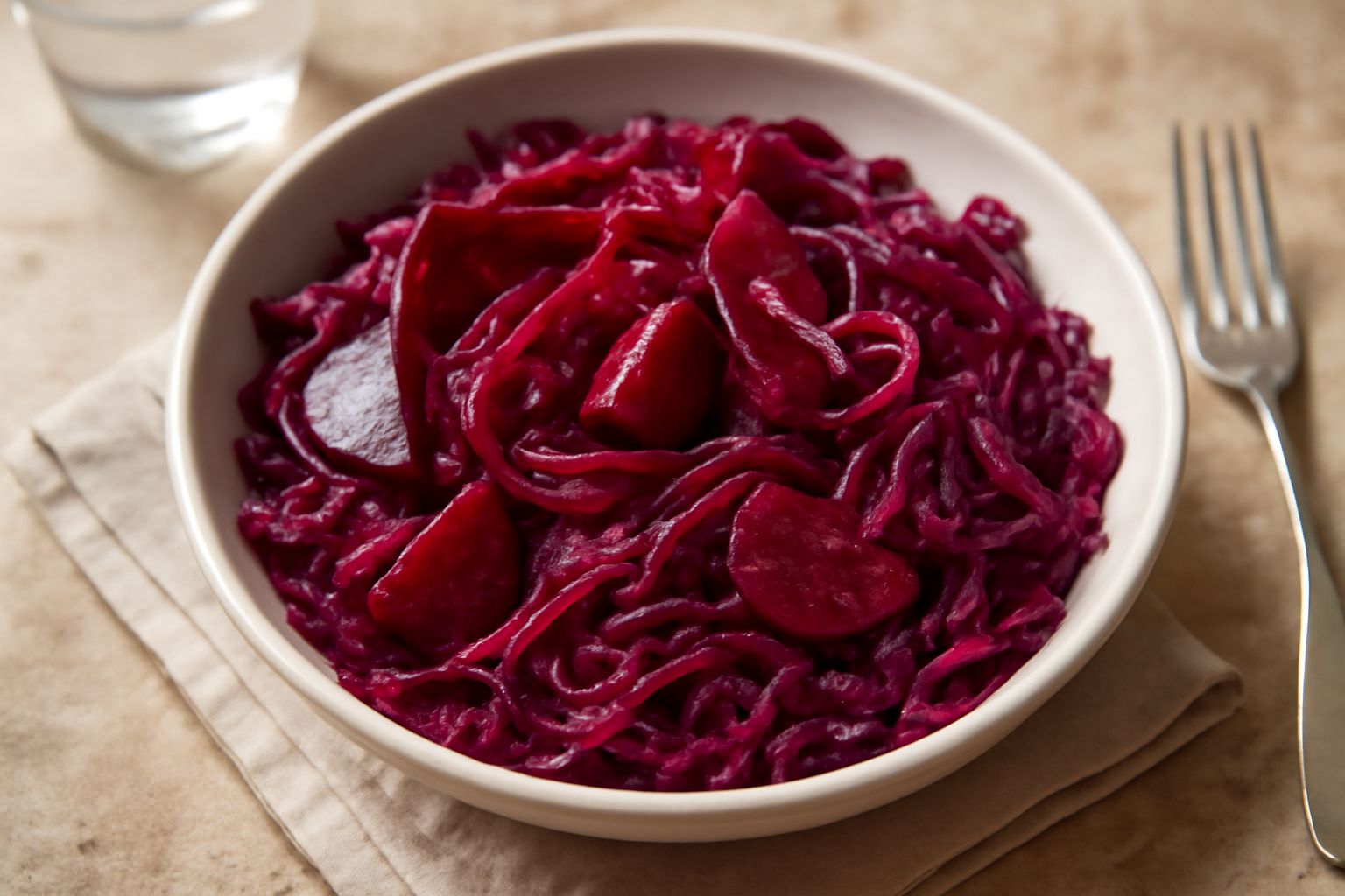 Insalata in ciotola bianca con cavolo rosso affettato sottile, barbabietole a julienne di colore rosso intenso, guarnita con semi di girasole e servita su tavolo di legno rustico