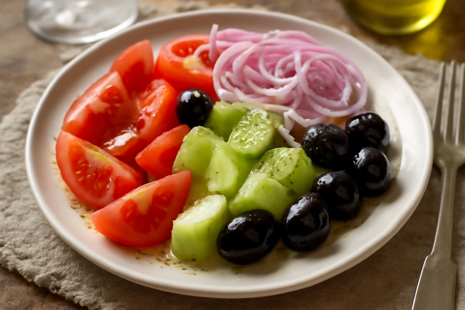 Insalata mista in piatto bianco con pomodori rossi tagliati a spicchi, fette di cetriolo verde, cipolla rossa sottile, olive nere e verdi, foglie di insalata mista, condita a lucido con olio d'oliva t