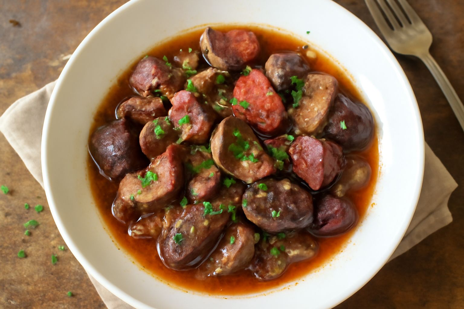 Interiora risuolate in un piatto bianco, pezzi rossi e marroni rosolati, cipolla dorata, salsa color mattone, prezzemolo fresco spolverato, contorno di insalata verde