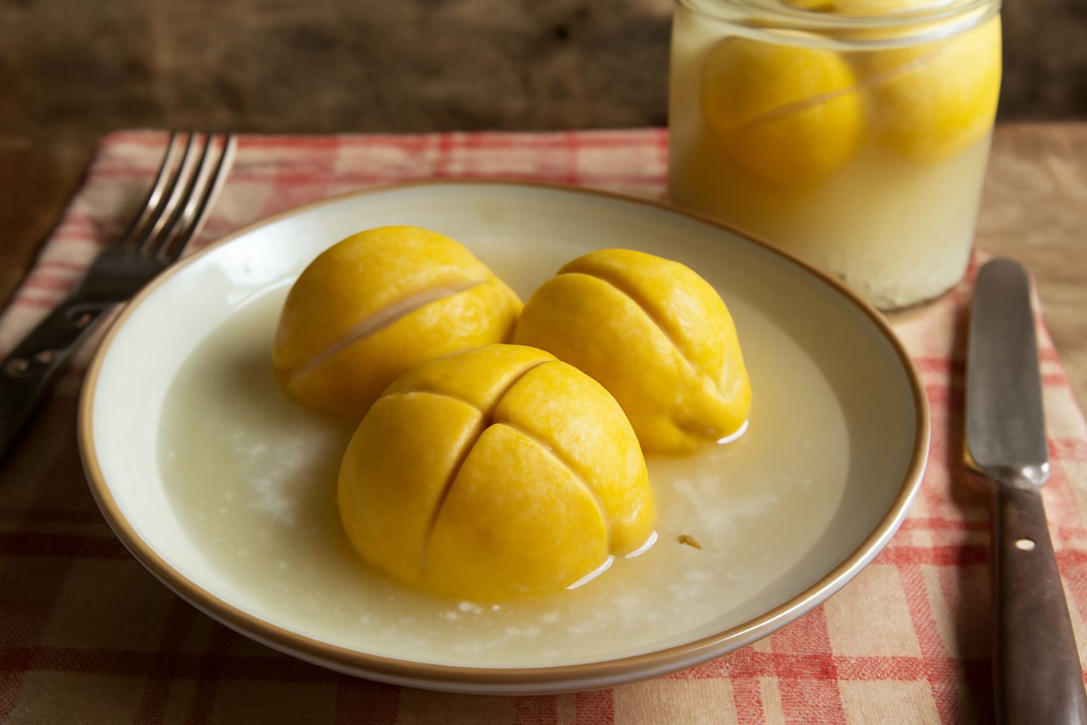Barattolo di vetro con limoni gialli interi o tagliati a metà in salamoia salata, su uno sfondo bianco da cucina, con foglie di limone accanto