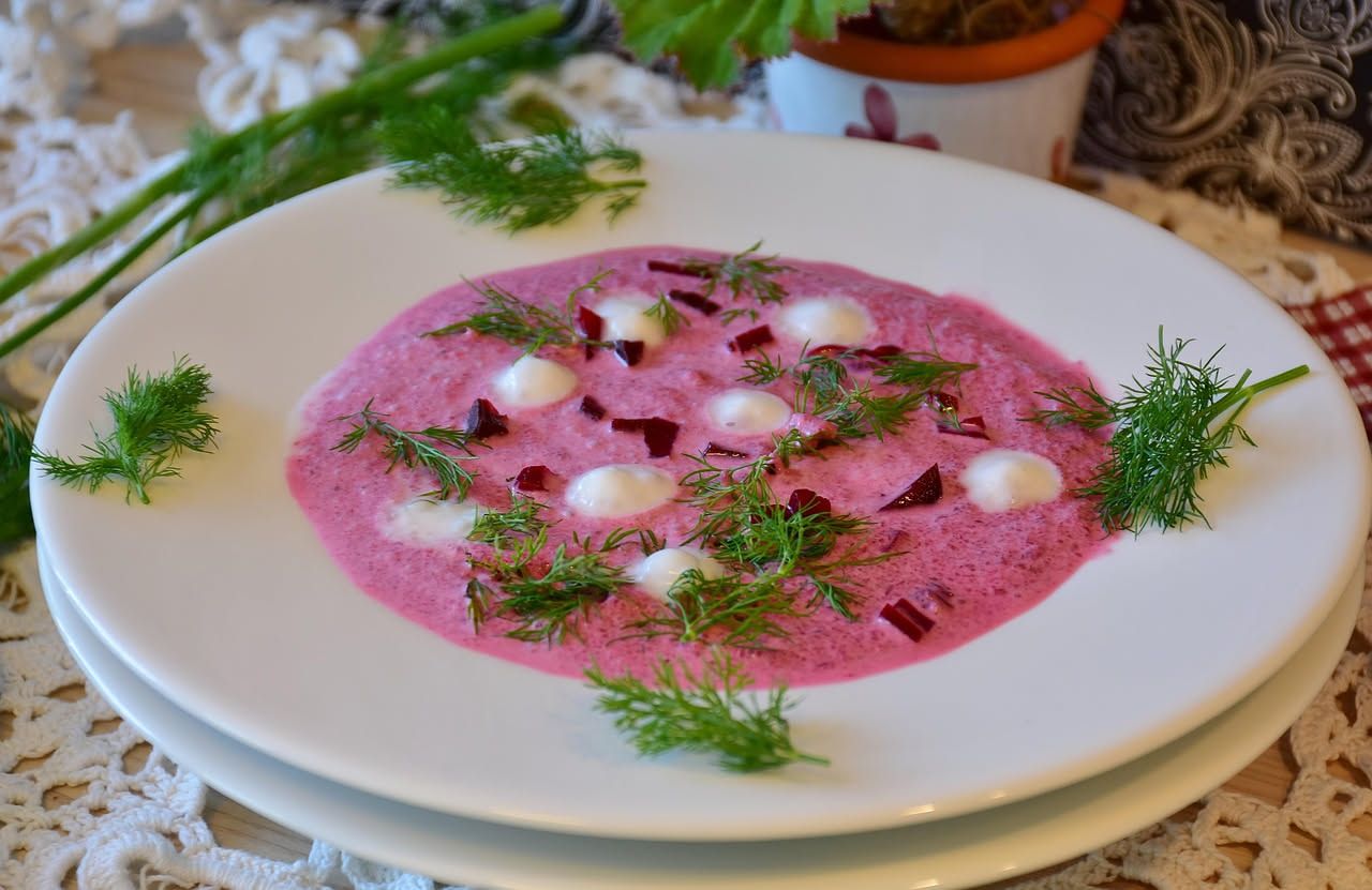 Fette di lingua salmistrata rosa e tenera su un piatto bianco, contornate da verdure di cottura e salsa rossa piccante in una ciotola