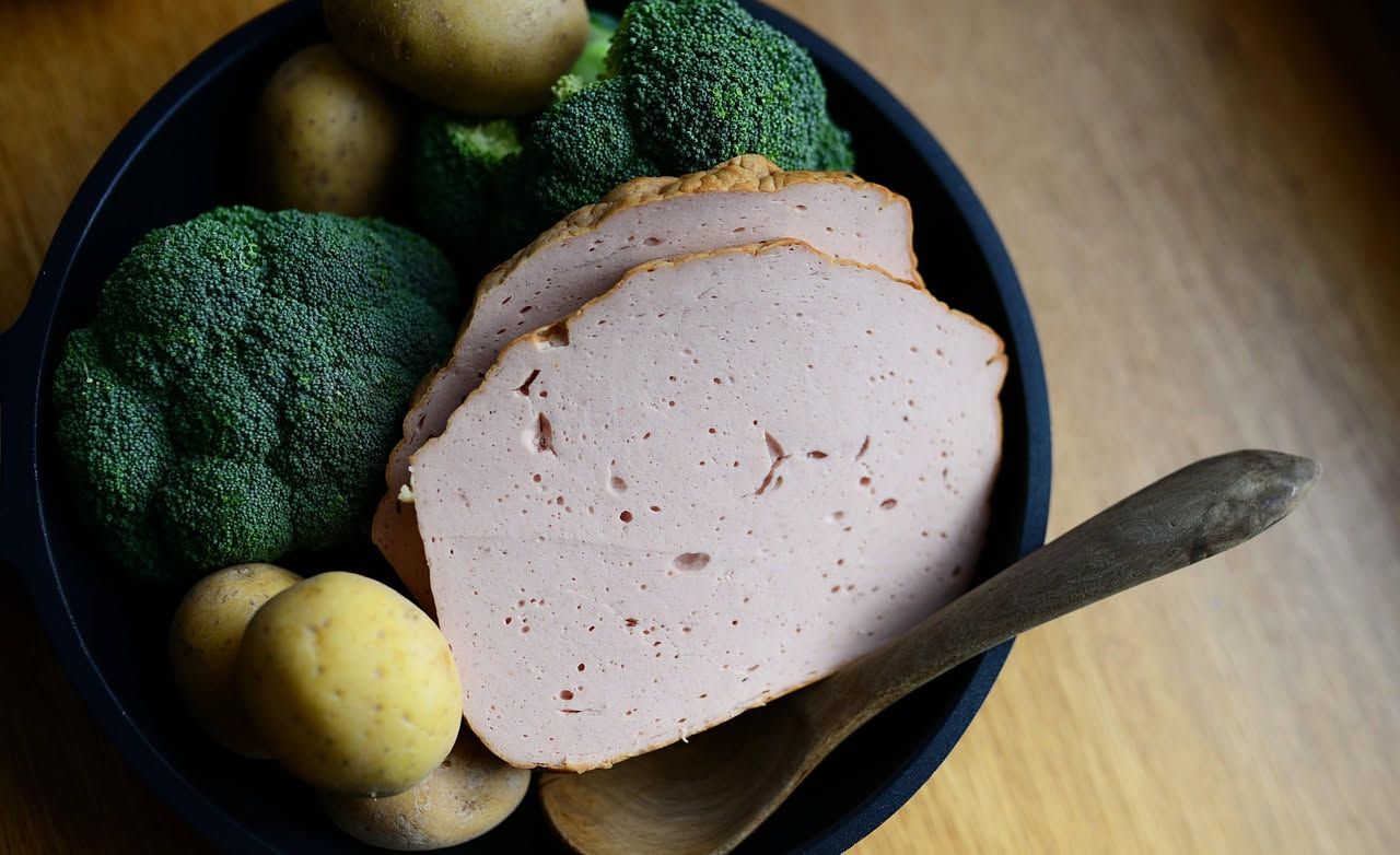 Mortadella di Modena tagliata a fette sottili disposte a ventaglio su un piatto bianco, con pistacchio visibile sulla superficie, accanto a pane toscano e olive verdi