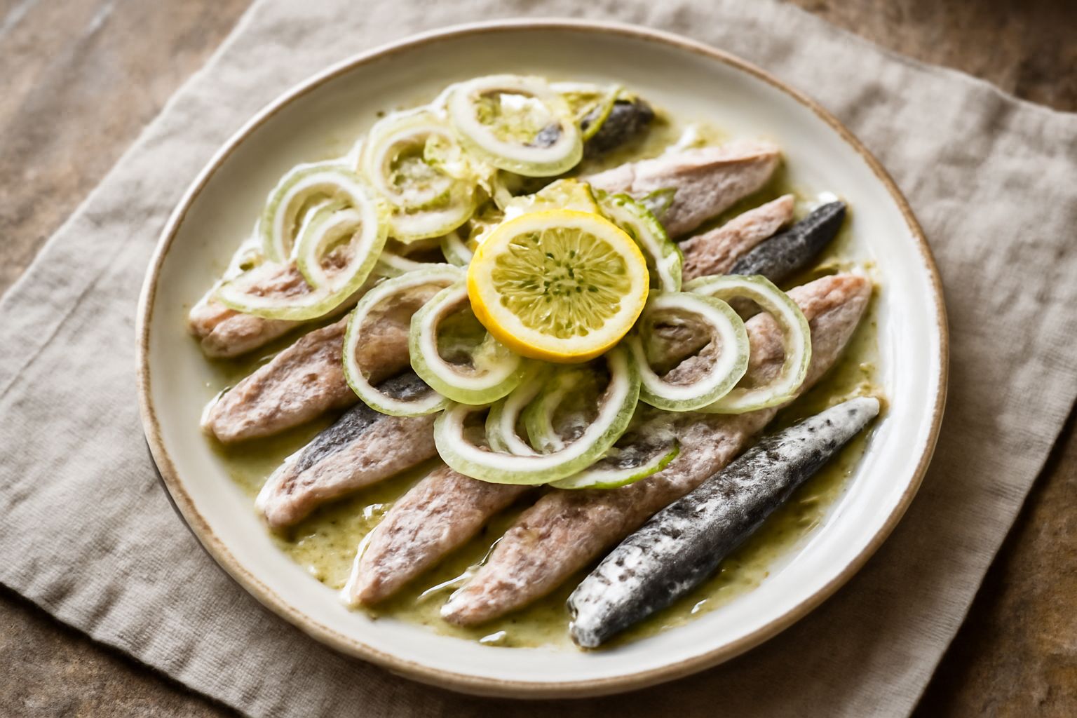 Fette di muggine marinato su un piatto bianco, ricoperte di marinata ambrata con spicchi di cipolla, erbe fresche e gocce di olio