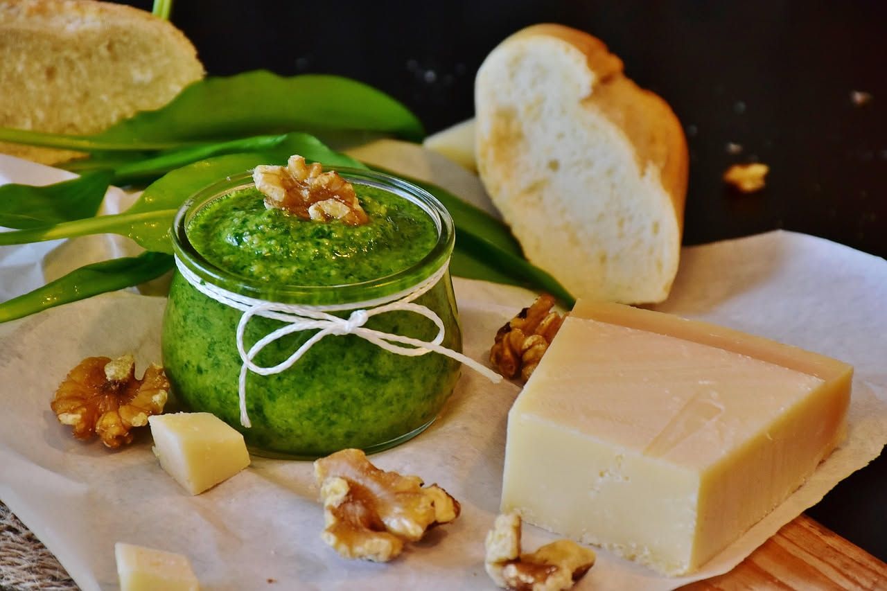 Noci tostate dorate accanto a cubetti di formaggio bianco su un tavolo di legno, con un bicchiere di vino bianco sfocato sullo sfondo