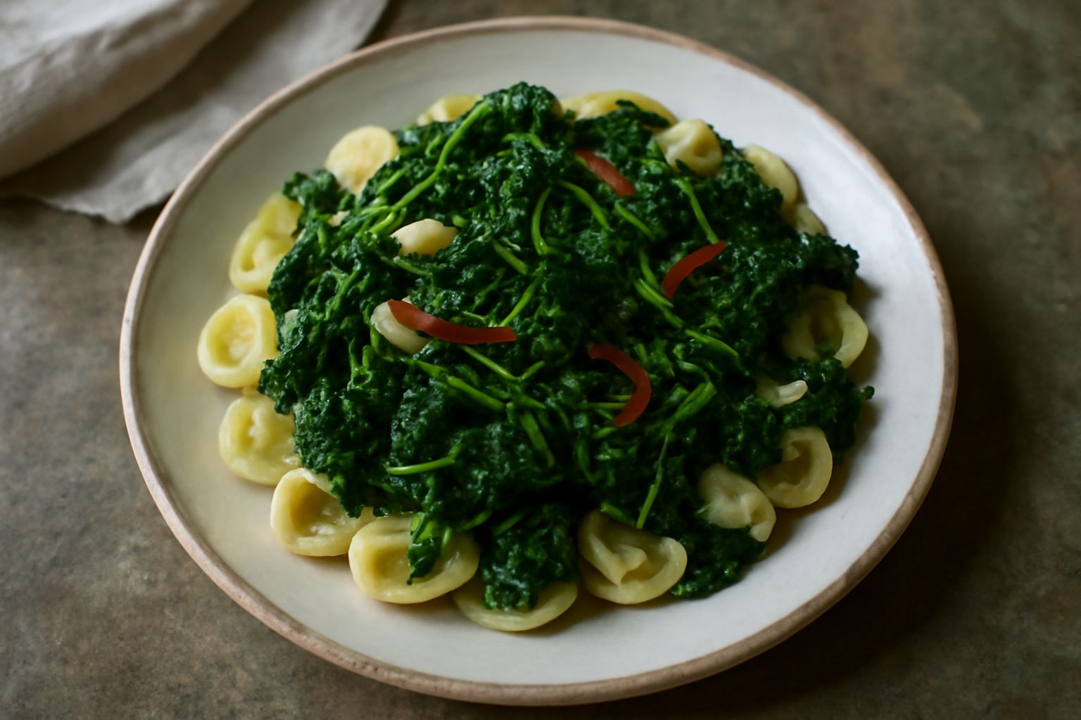 Piatto di orecchiette di pasta fresca condite con cime di rapa verdi scuro, aglio dorato e gocce di olio, servite in ciotola di ceramica bianca con forchetta