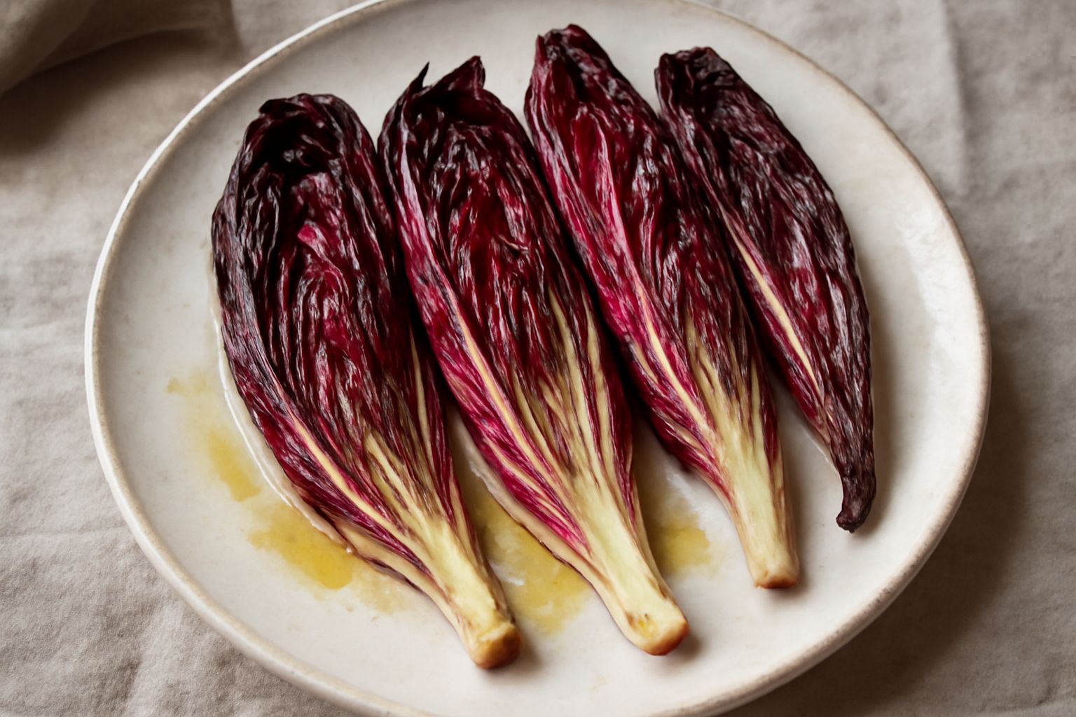 Radicchio rosso di Treviso tagliato a spicchi, dorato ai bordi nel piatto bianco, condito con olio d'oliva lucido e fettine di limone giallo, su sfondo grigio